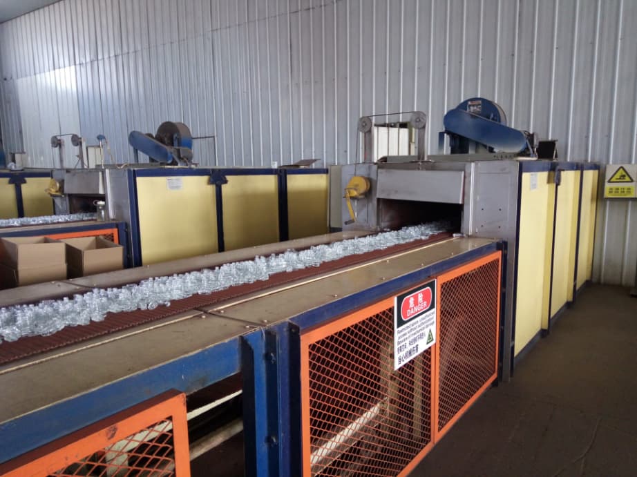Container glass production: bottles leaving the annealing lehr – a specialized, long oven used to cool newly formed glass gradually and remove internal mechanical stresses 
